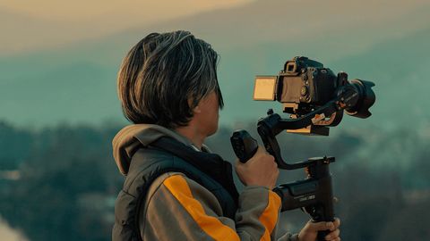 Person filming a misty hillside landscape at sunset with a camera on a handheld gimbal
