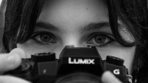 Black and white close-up of a woman's eyes peering over the top of a Lumix camera